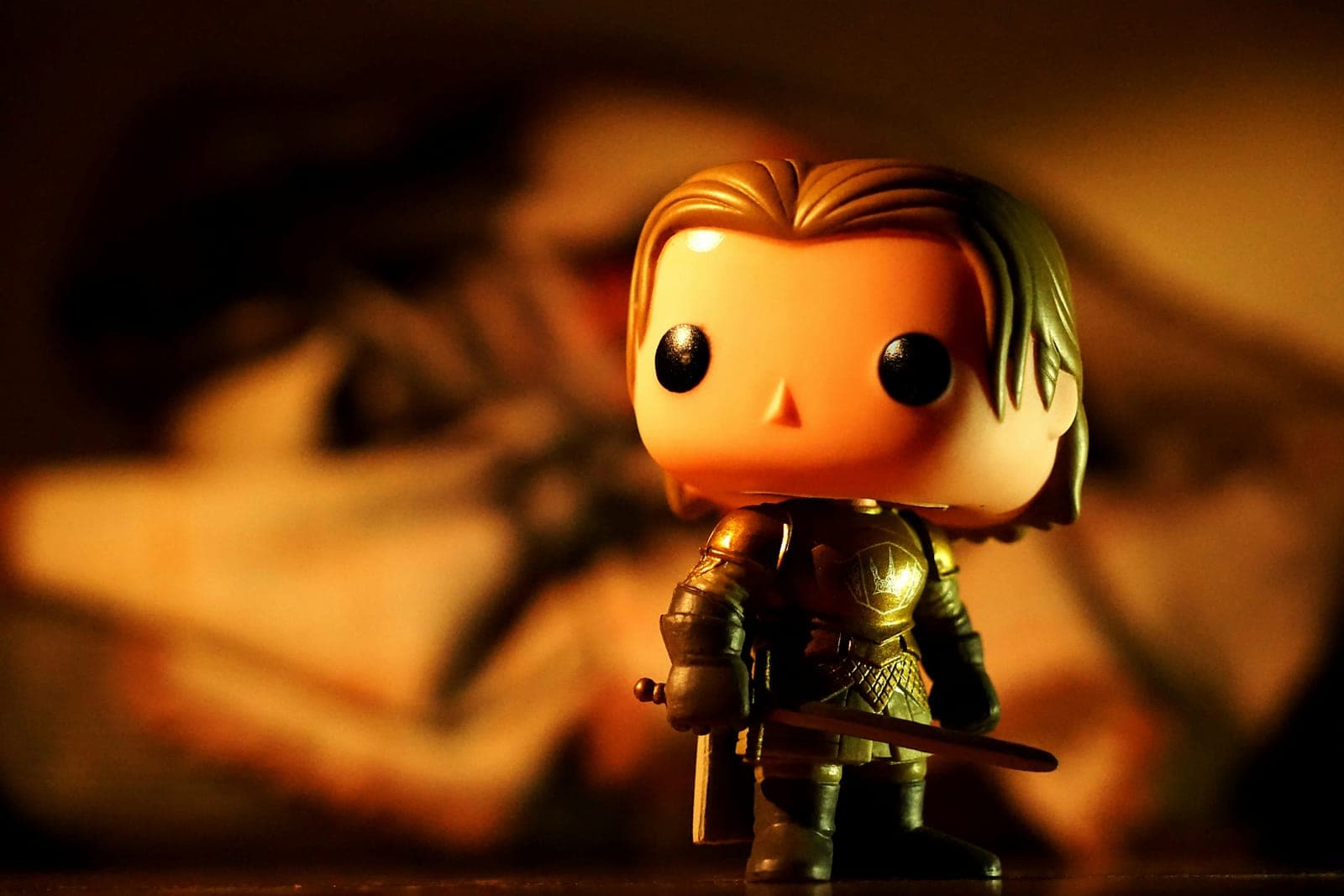 A small vinyl figure of an armored knight holding a sword, lit in warm orange light.